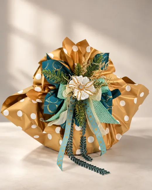 Confezione a sacchetto in carta oro a pois bianchi, chiusa con nastri verde petrolio e celeste, rametti di pino e un fiore crema