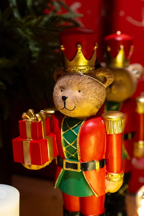 Un orsetto schiaccianoci con la corona d'oro e la giubba rossa e verde, con in mano un pacco regalo rosso