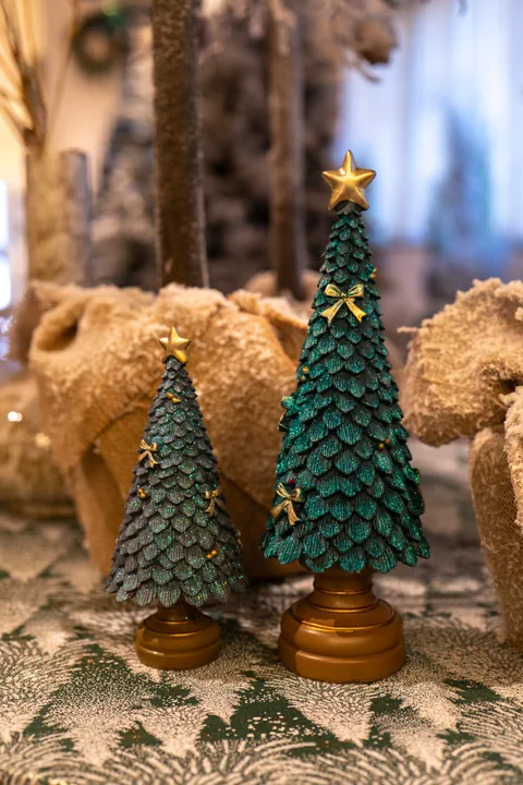 Due alberelli verde petrolio con la stella d'oro su basi dorate, fra decorazioni in peluche color sabbia