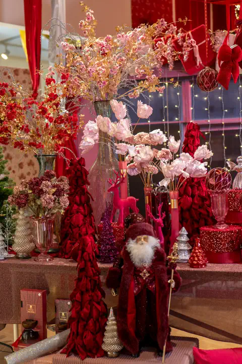 Angolo bordeaux dello showroom: alberelli di petali bordeaux, un Babbo Natale in velluto bordeaux e rami fioriti rosa cipria in vasi di vetro