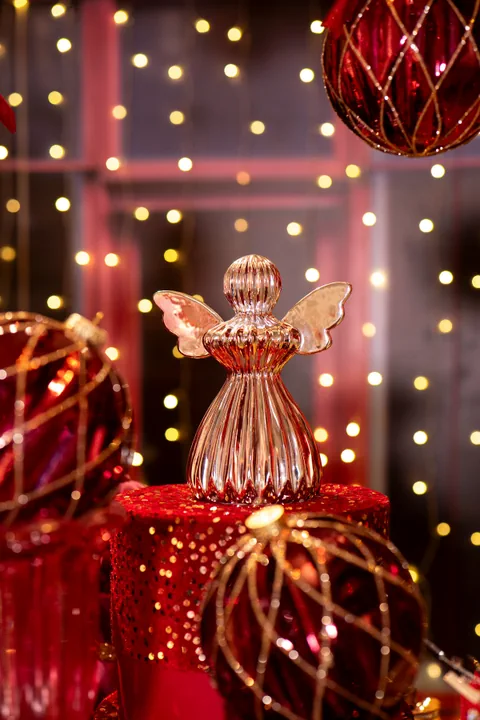 Un angelo in vetro rosa e oro fra sfere di vetro bordeaux con la rete oro e luci accese
