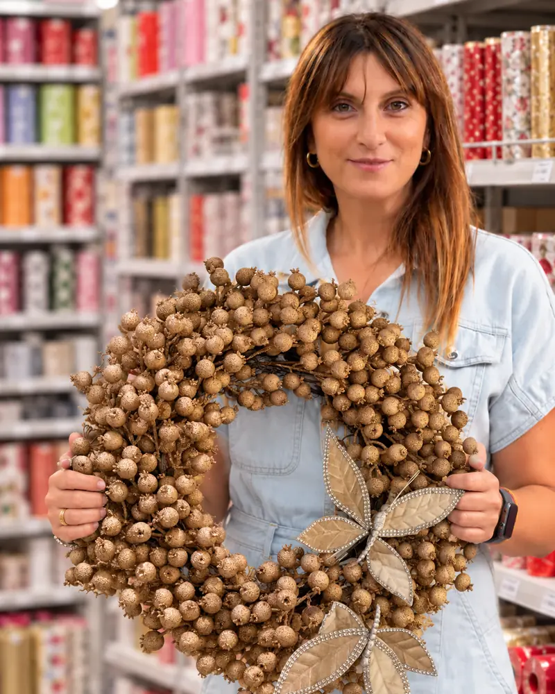 Maria Vittoria Sampaolo tiene una ghirlanda di bacche champagne con due farfalle in velluto e strass, della collezione Serra Liberty, tra gli scaffali di carte da regalo dello showroom